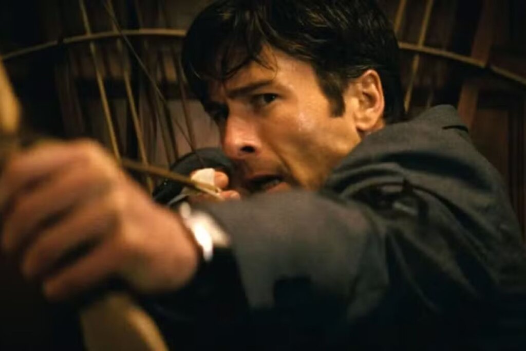 Cena do filme "Manual Prático Da Vingança Lucrativa", com o ator Glen Powell segurando um arco e flecha 