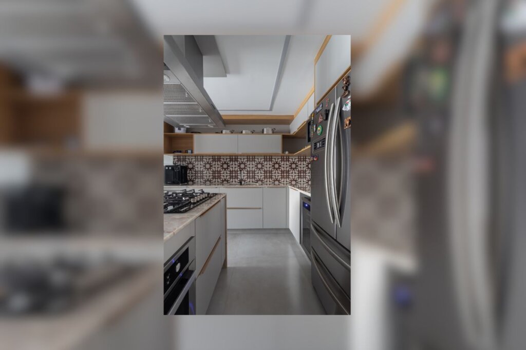 Cozinha com revestimento geométrico marrom e branco, móveis brancos e geladeira cinza