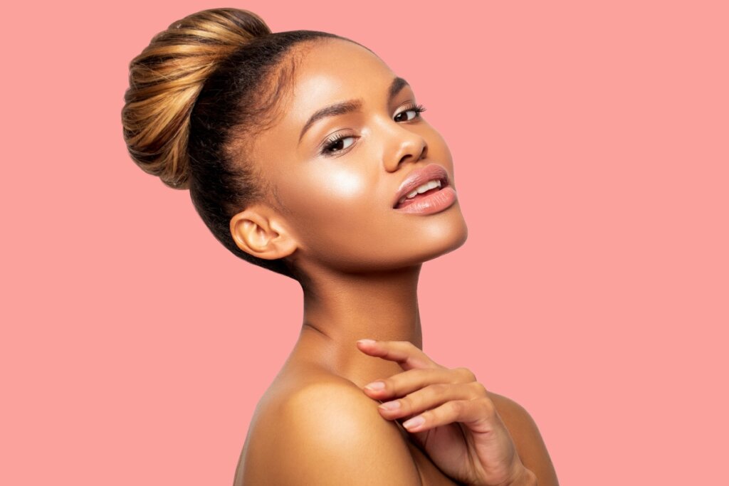 Mulher com cabelo preso em coque alto, olhando para a câmera, em fundo rosa