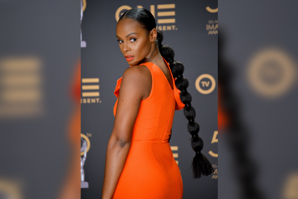 Mulher com cabelo com penteado bubble ponytail, usando vestido laranja, virada de costas e olhando para trás