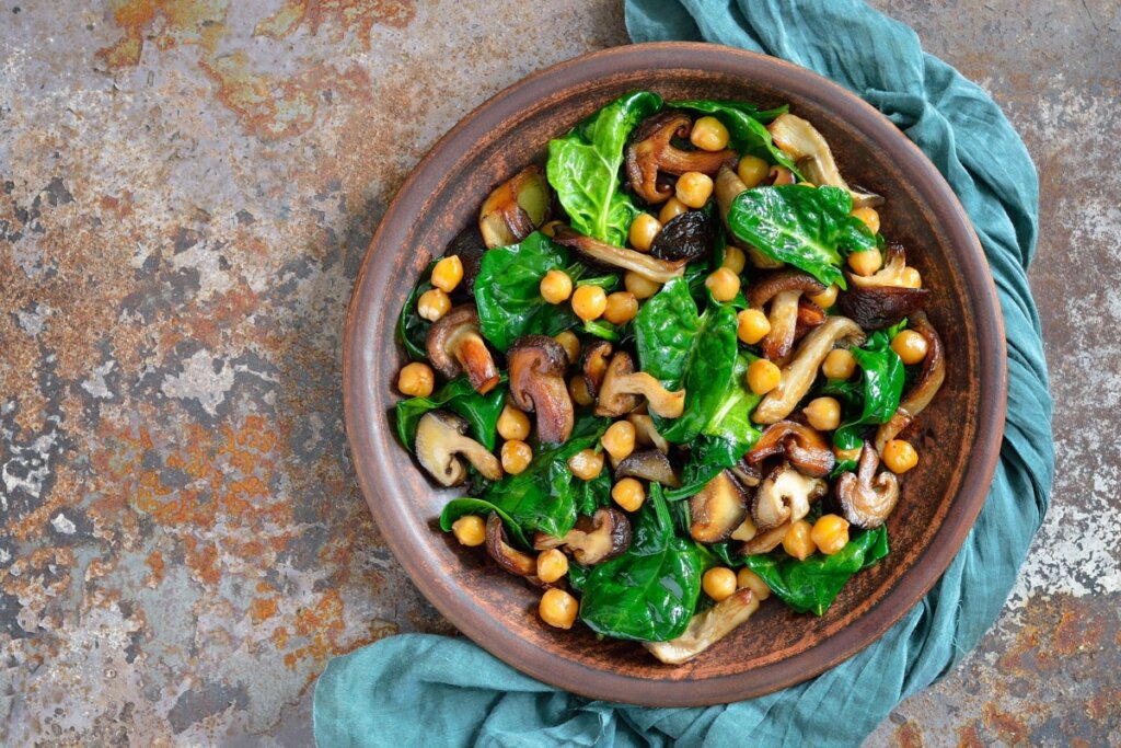 Salada morna de grão-de-bico com cogumelo e espinafre servido em tigela de cerâmica em cima de bancada de pedra