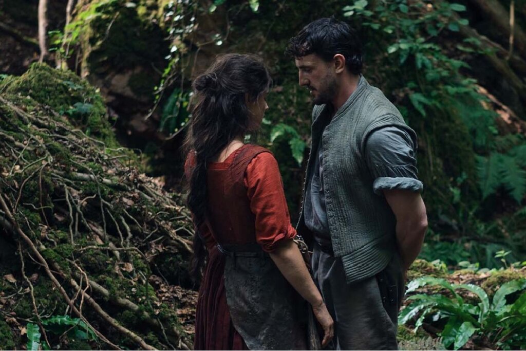 Cena do filme "Hamnet - A Vida Antes de Hamlet" , com um casal um de frente para o outro em uma floresta 