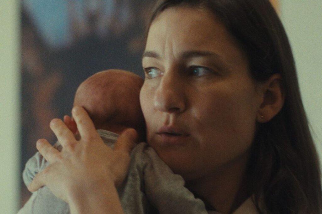 Cena do filme "Mother's Baby", com a protagonista segurando um bebê e olhando para o lado