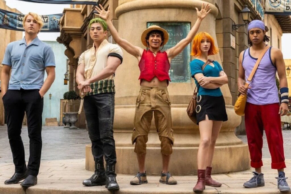 Os cinco membros principais da tripulação dos Piratas do Chapéu de Palha posam em frente a uma estrutura circular de pedra. Ao centro, Luffy usa seu chapéu de palha e colete vermelho com os braços abertos. Ao lado dele estão Zoro (cabelo verde), Nami (cabelo laranja), Sanji (cabelo loiro) e Usopp (lenço roxo na cabeça), todos caracterizados com suas roupas clássicas da série live-action.