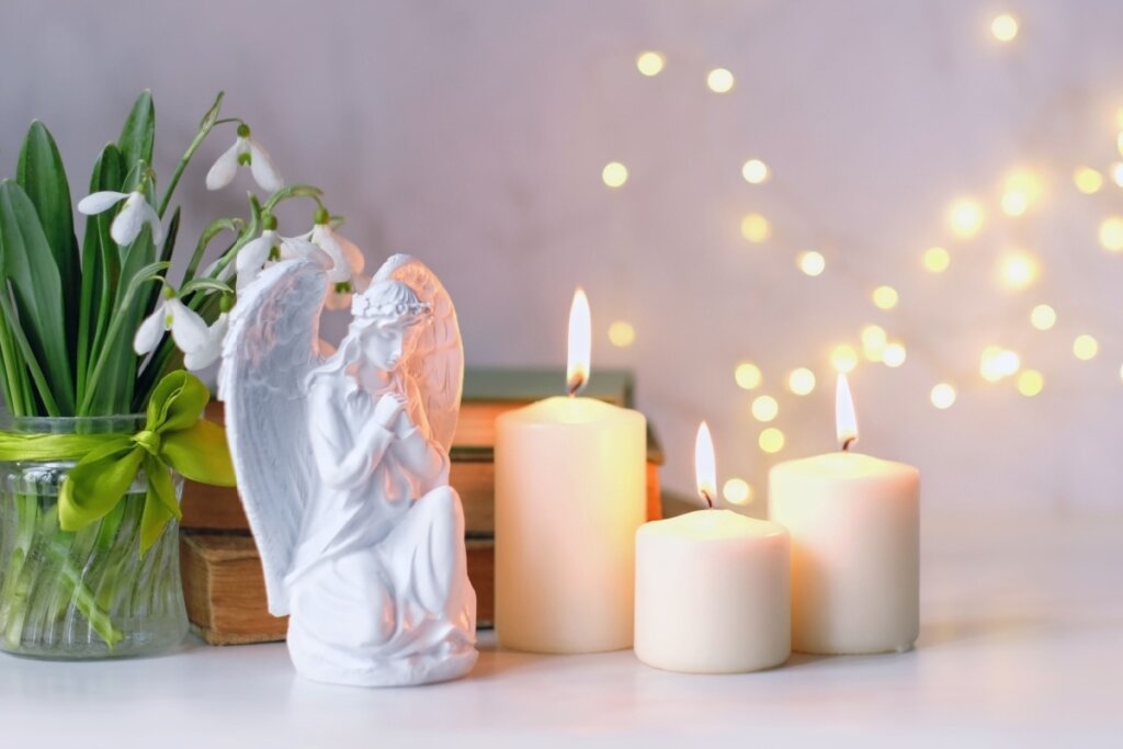 imagem da estátua de um anjo branco rezando ao lado de três velas brancas acesas
