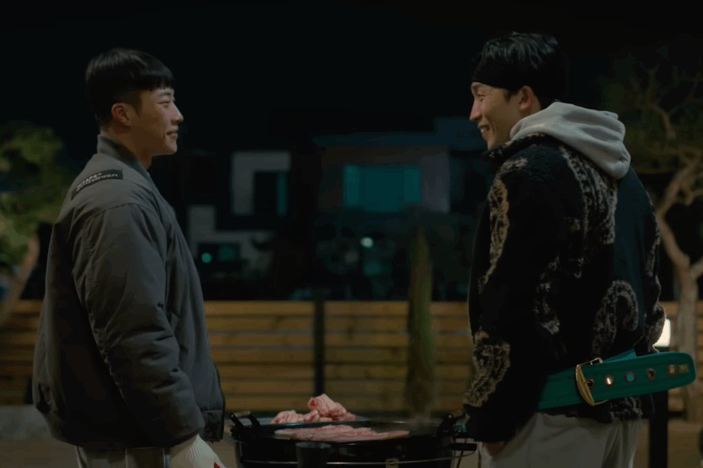 Dois homens conversando e sorrindo enquanto preparam comida em uma grelha à noite