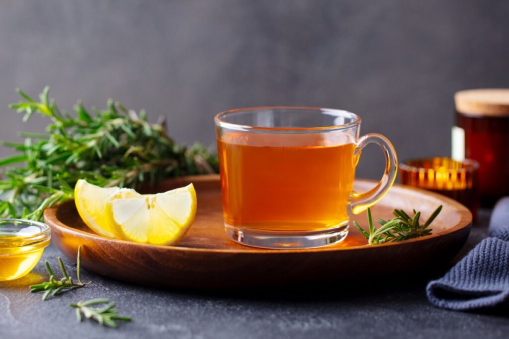 Xícara de vidro com chá marrom em cima de um prato marrom com rodelas de limão 