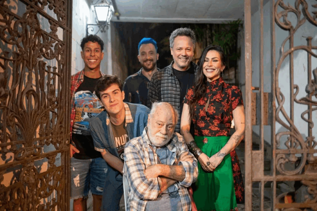 Grupo de pessoas posando para foto, com senhor de idade sentado a frente de braços cruzados e um casal e três jovens