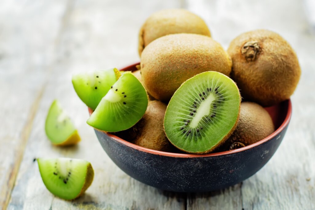 Cumbuca com kiwis, com uma metade cortada e a outra metade cortada em gomos.
