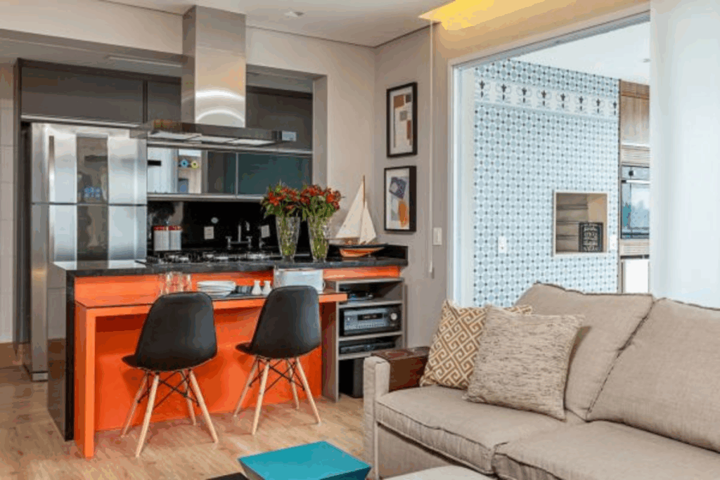Cozinha com bancada com móvel laranja, duas cadeiras pretas e sofá bege 