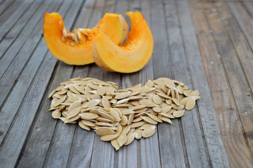 Sementes de abóbora organizadas em formato de coração sobre uma superfície de madeira, com pedaços de abóbora ao fundo