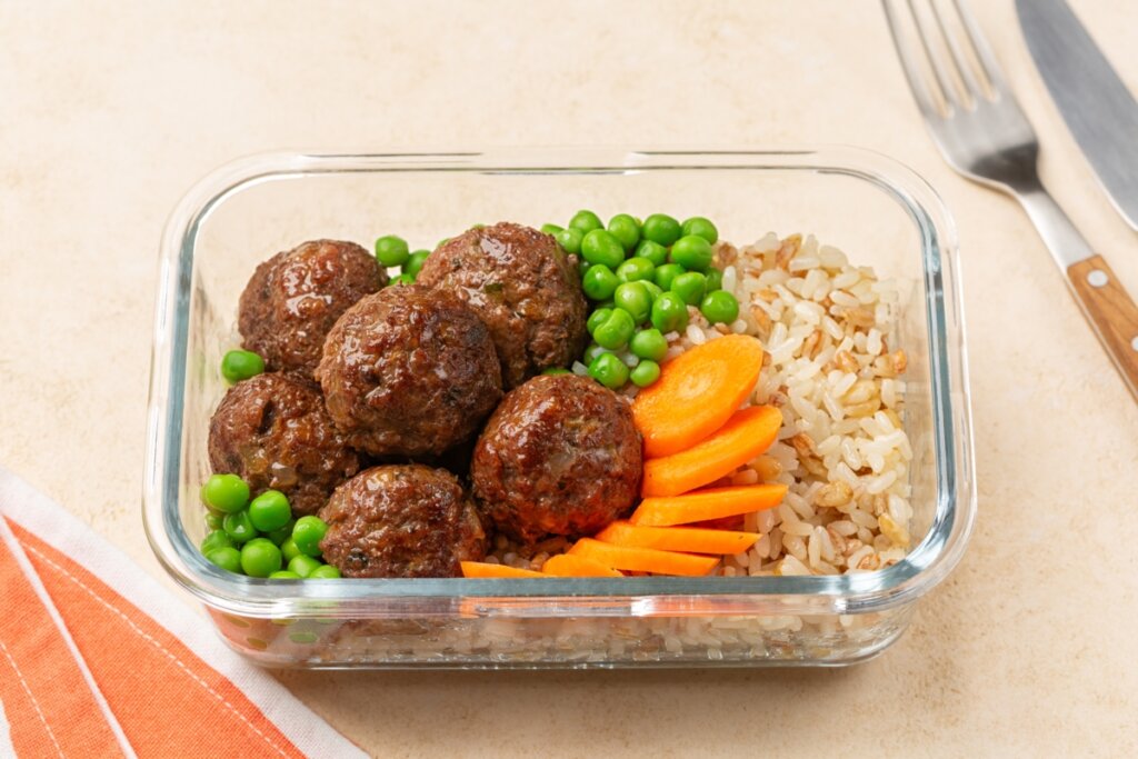 Almôndegas com arroz integral, ervilha e cenoura em uma marmita de vidro 
