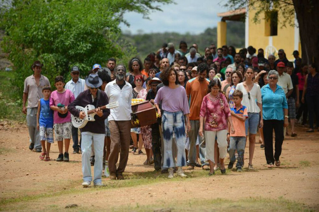 Diversas pessoas carregando um caixão e acompanhando um cortejo
