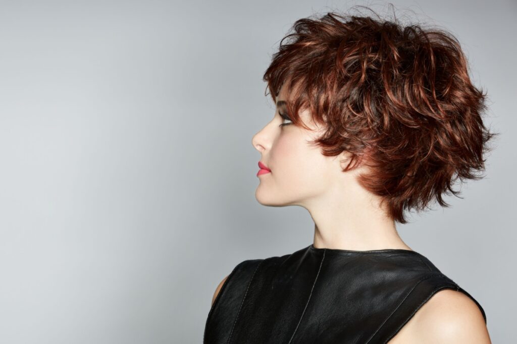 Mulher ruiva, com corte pixie, virando de lado e usando vestido preto